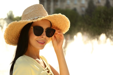 Photo of Beautiful young woman wearing stylish sunglasses outdoors. Space for text