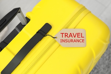 Photo of Yellow suitcase with TRAVEL INSURANCE label on floor, top view