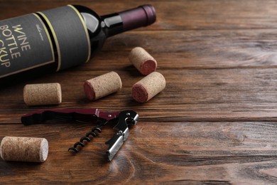 Photo of Corkscrew, wine bottle and stoppers on wooden table. Space for text