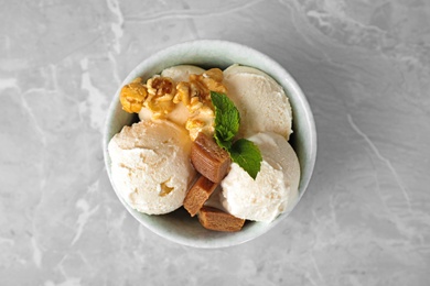 Photo of Bowl of delicious ice cream with caramel candies, popcorn and mint on light grey marble table, top view