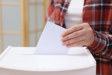 Photo of Woman putting her vote into ballot box on blurred background, closeup