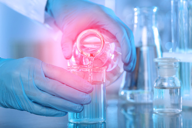 Image of Scientist pouring liquid into beaker at table, closeup. Laboratory analysis