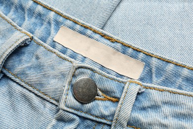 Photo of Blank clothing label on light blue jeans, top view