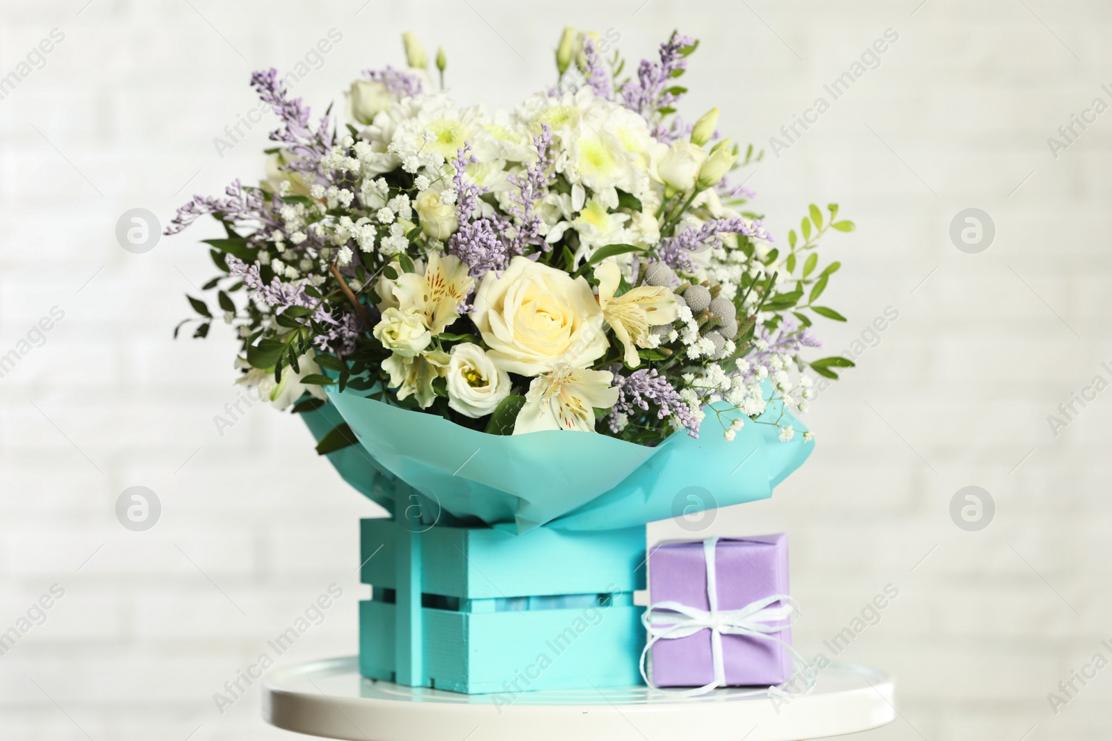 Photo of Beautiful bouquet of flowers in decorative crate and gift box on table against light background