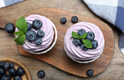 Photo of Sweet cupcakes with fresh blueberries on wooden table, flat lay