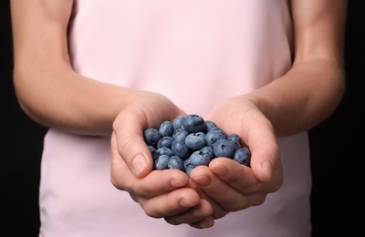 Photo of Woman holding juicy fresh blueberries, closeup view