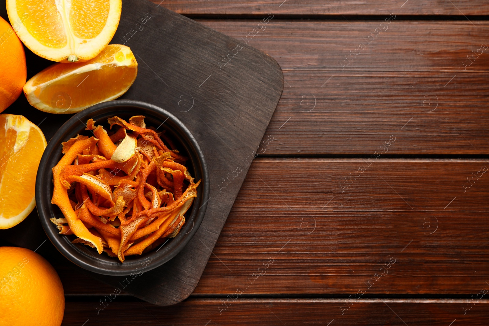 Photo of Bowl with dry orange peels and fresh fruits on wooden table. Space for text