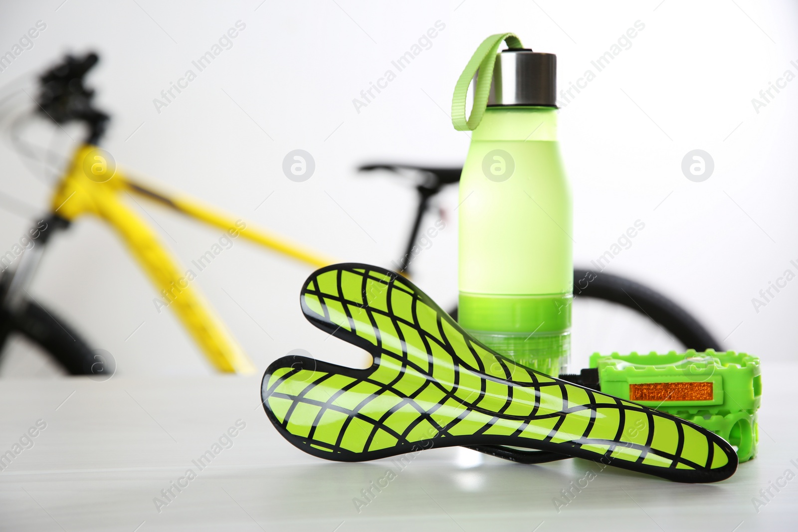 Photo of Bicycle saddle, bottle and pedals on white table. Space for text