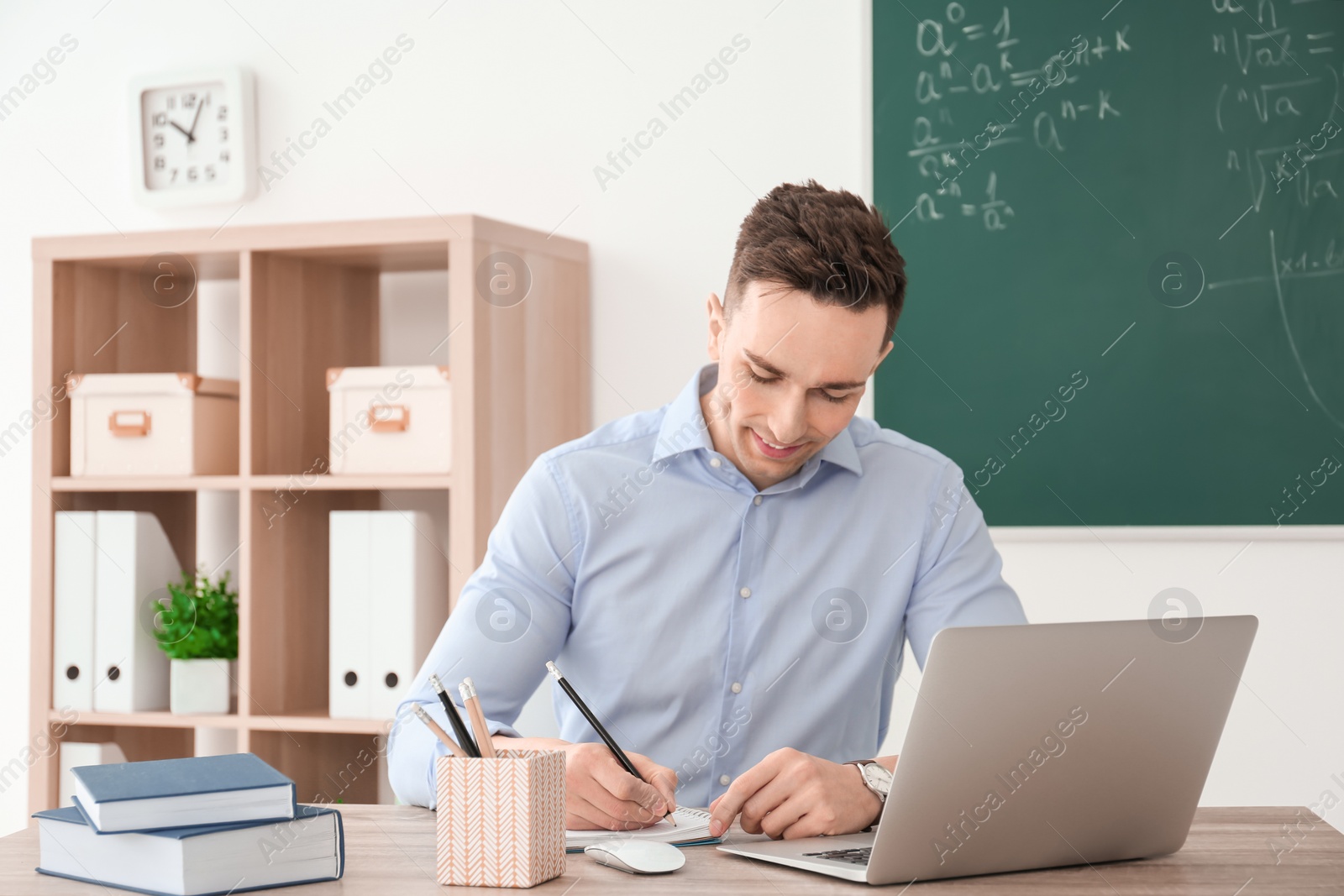 Photo of Young male teacher working at table in classroom