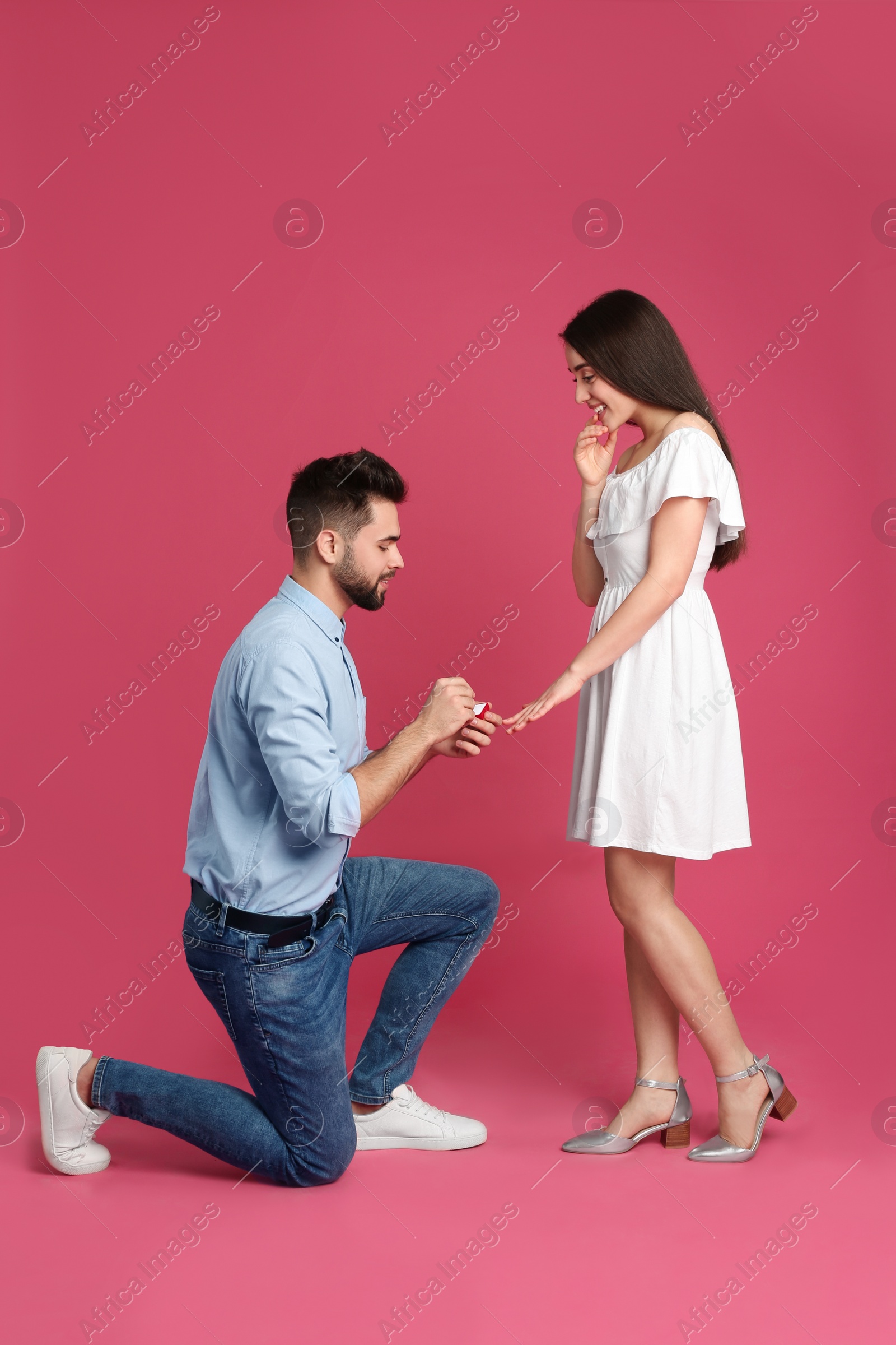 Photo of Man with engagement ring making marriage proposal to girlfriend on crimson background