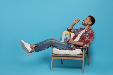 Photo of Handsome man eating potato chips on light blue background