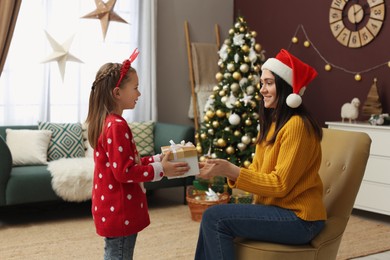 Photo of Daughter giving gift to her mother in room decorated for Christmas