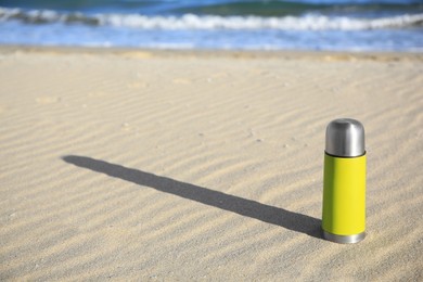 Yellow thermos with hot drink on sand near sea, space for text