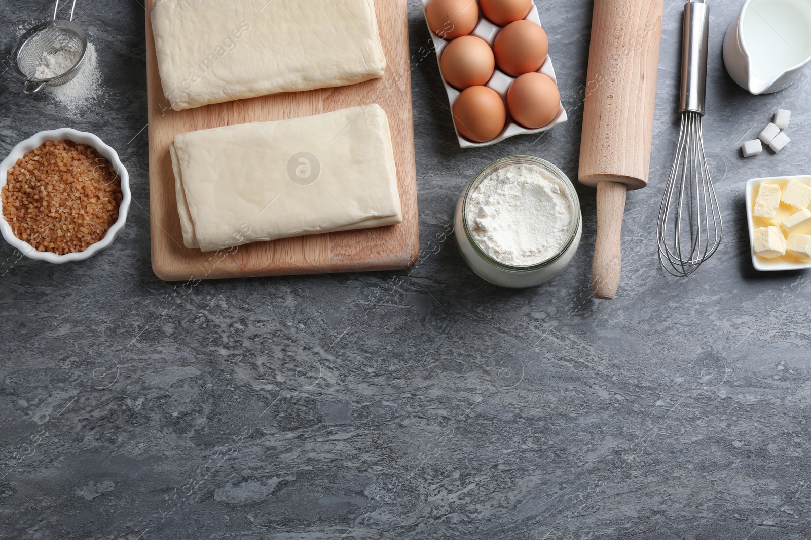 Photo of Puff pastry dough and ingredients on grey table, flat lay. Space for text