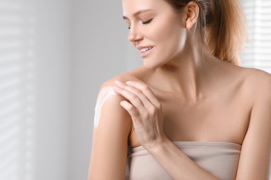 Beautiful woman applying body cream onto shoulder indoors, space for text