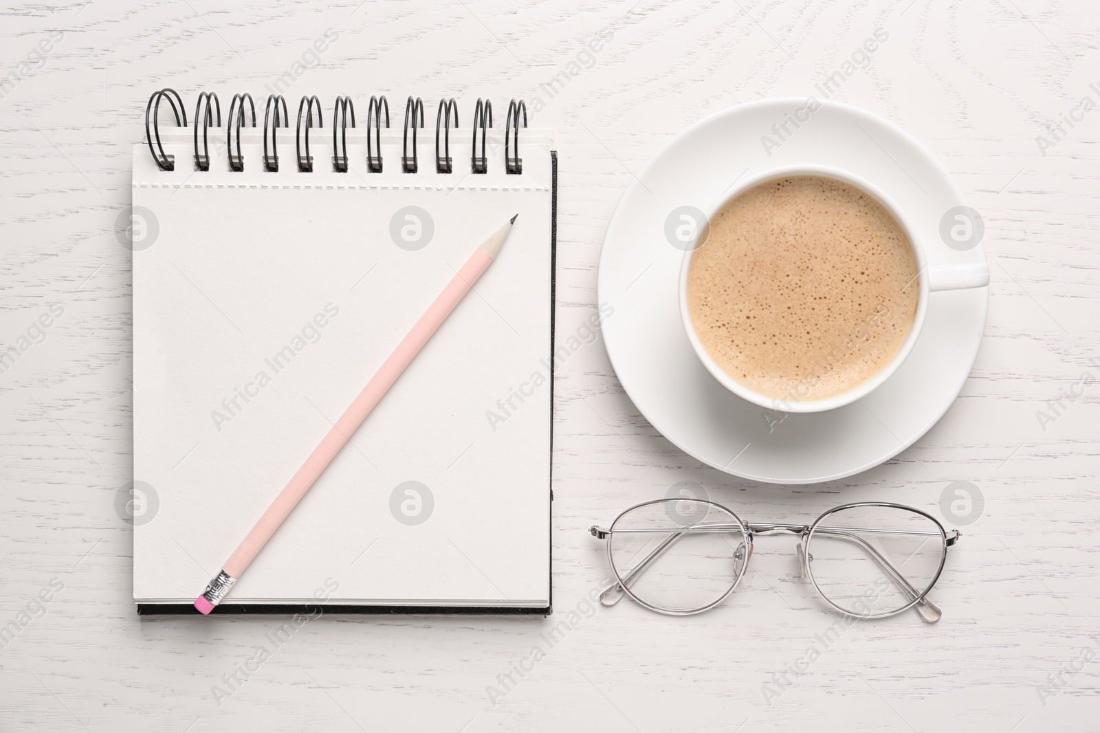 Photo of Notebook with pencil, glasses and cup of coffee on white wooden table, flat lay