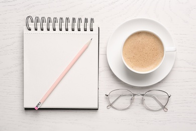 Photo of Notebook with pencil, glasses and cup of coffee on white wooden table, flat lay