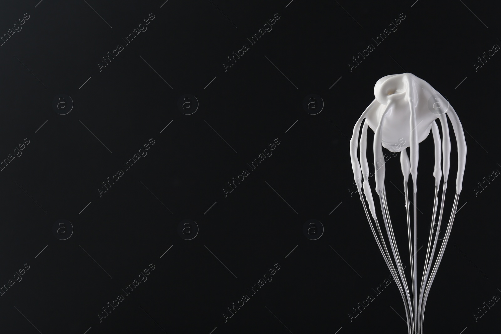 Photo of Whisk with whipped cream on black background. Space for text