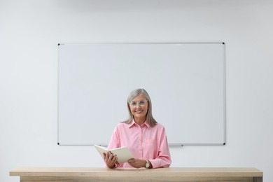 Photo of Professor with book sitting at desk in classroom