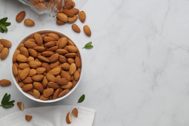 Photo of Bowl with delicious almonds and fresh leaves on white marble table, flat lay. Space for text