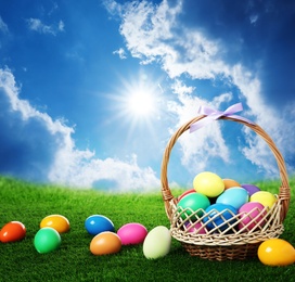 Image of Wicker basket with Easter eggs on green grass outdoors
