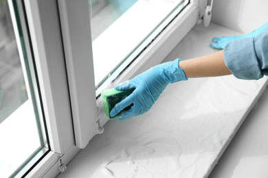 Photo of Woman cleaning window sill with sponge, closeup