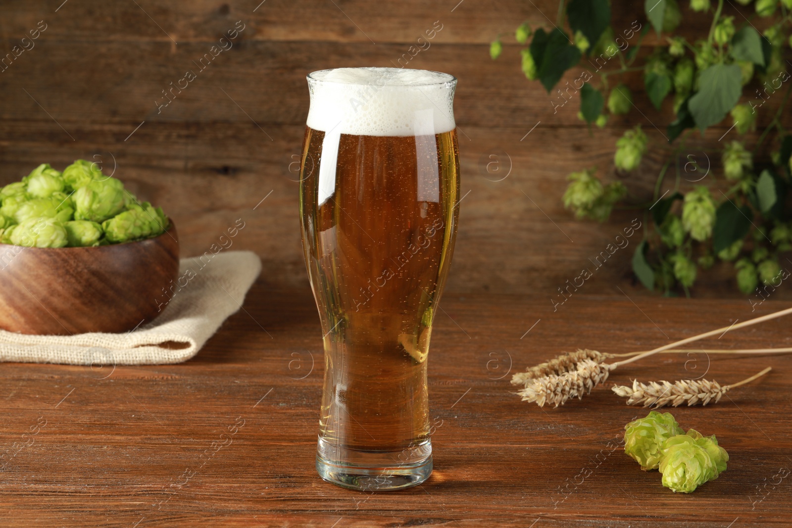 Photo of Glass of beer, fresh green hops and spikes on wooden table