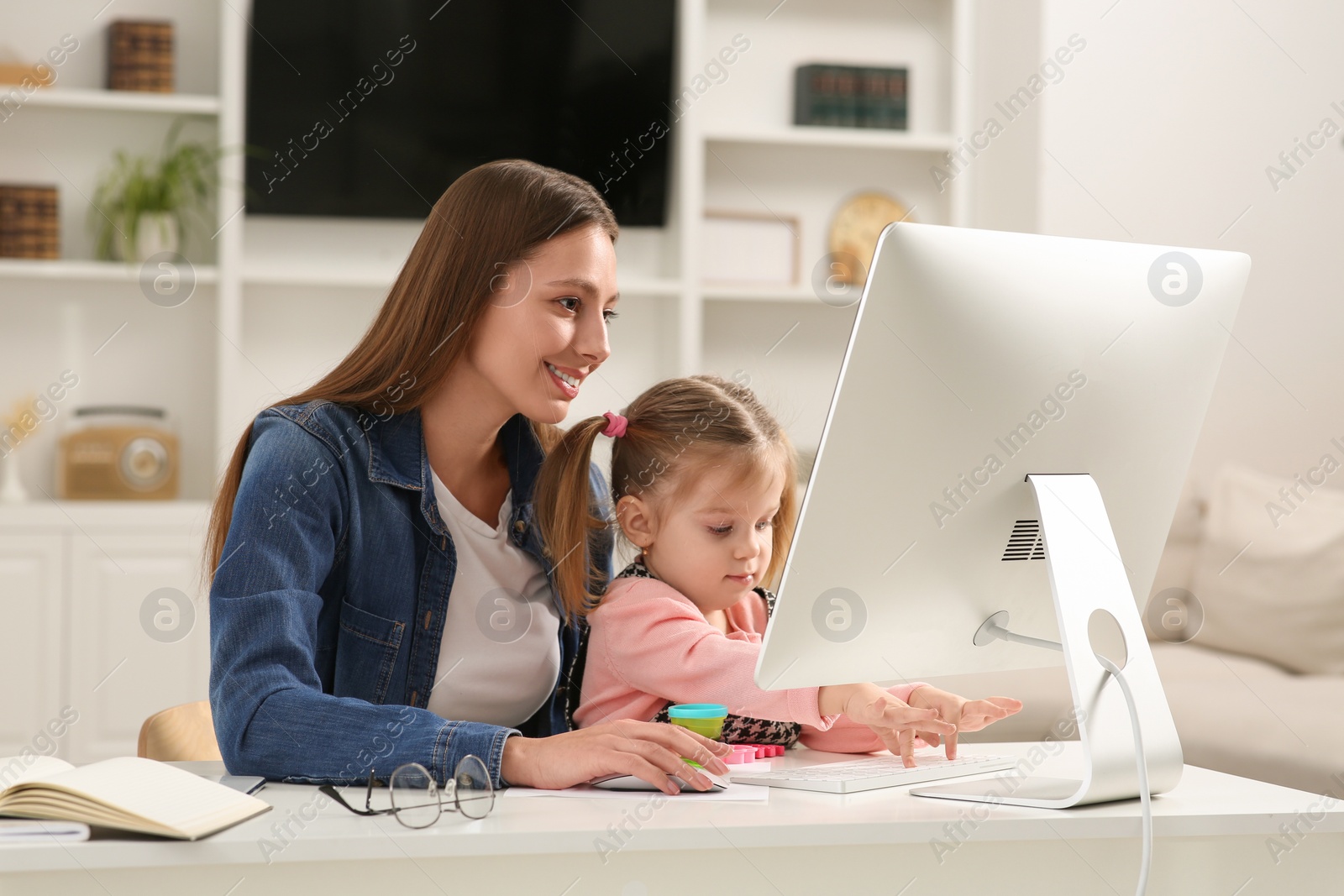 Photo of Woman working remotely at home. Mother and her daughter at desk with computer