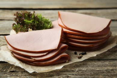 Slices of delicious boiled sausage with lettuce and spices on wooden table, closeup