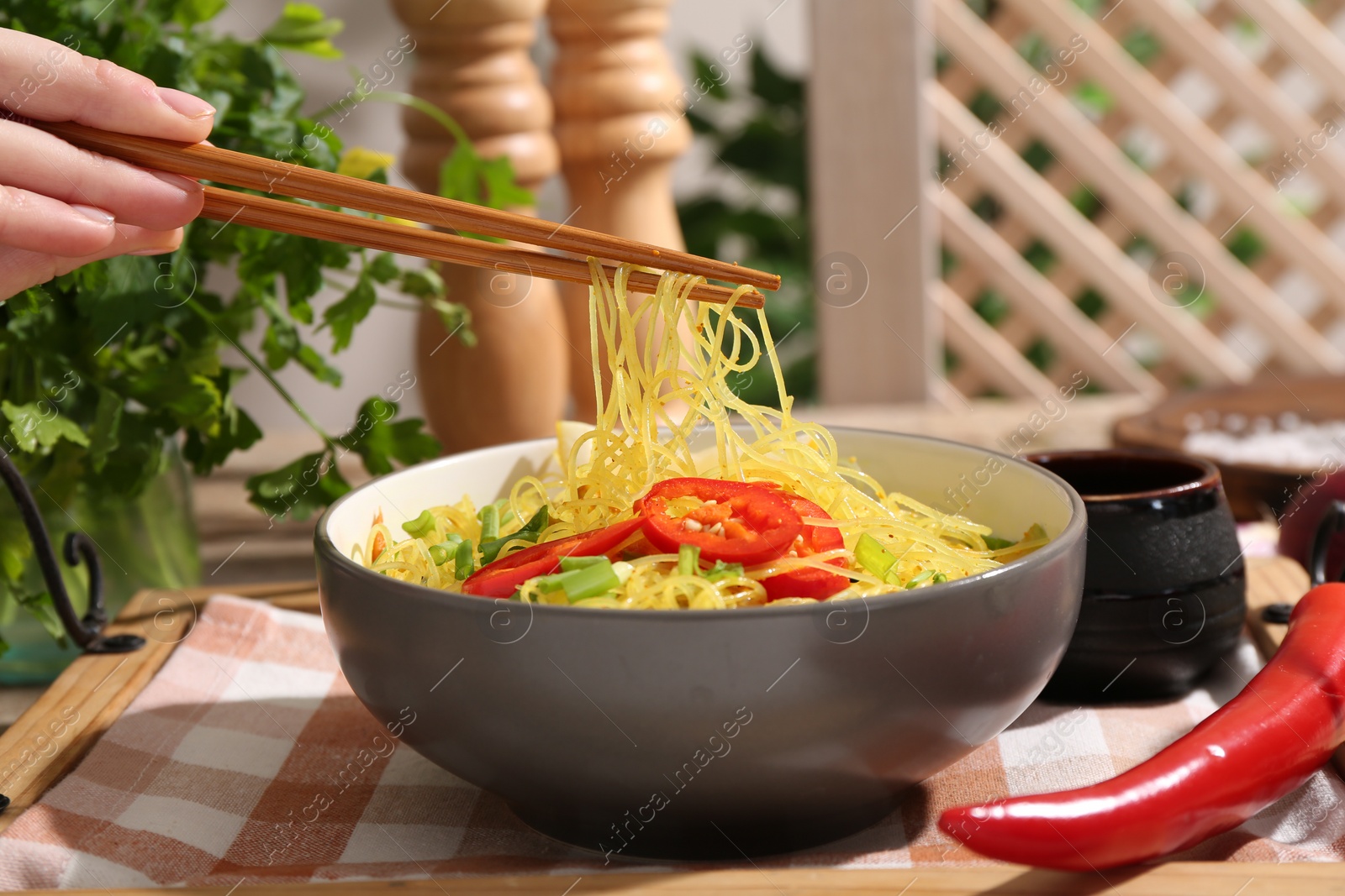 Photo of Stir-fry. Woman using chopsticks for eating tasty noodles with meat and vegetables at table, closeup