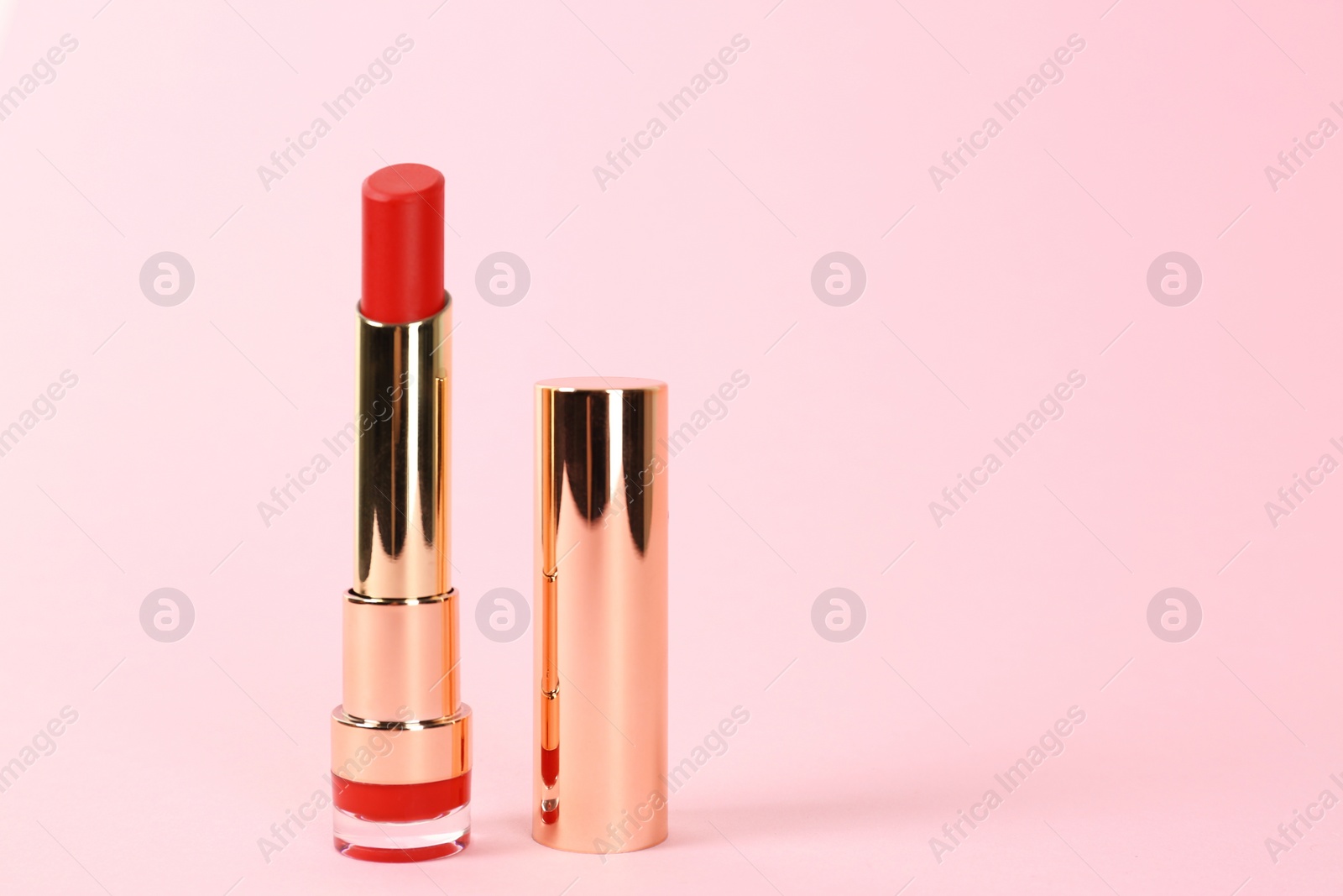 Photo of Bright lipstick in gold tube on pink background, space for text
