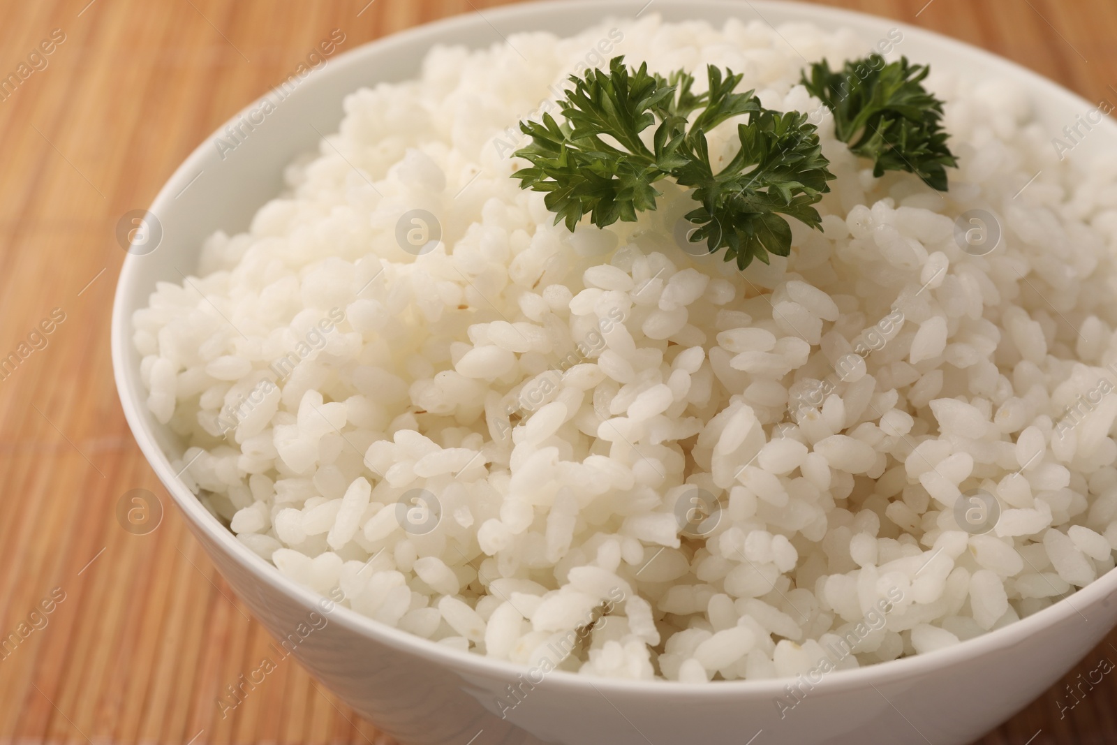 Photo of Bowl with delicious rice and parsley on bamboo mat, closeup