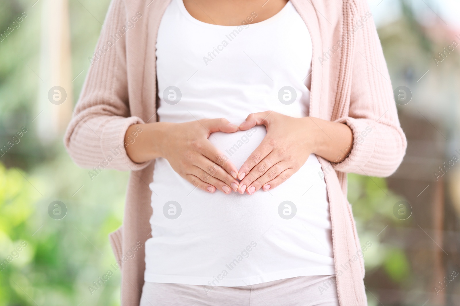 Photo of Pregnant woman standing near window at home, closeup