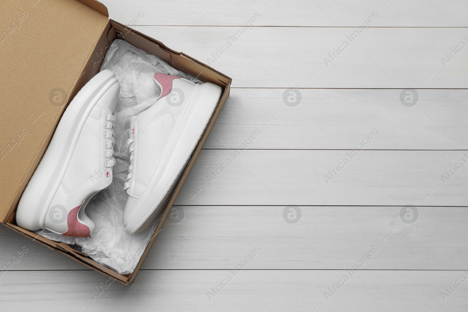 Photo of Pair of stylish sport shoes in cardboard box on white wooden background, top view. Space for text