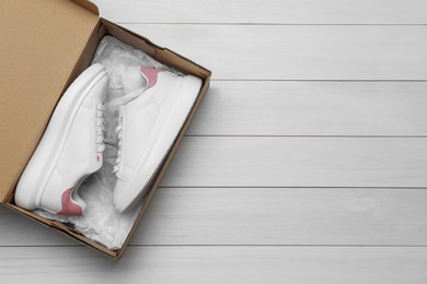 Photo of Pair of stylish sport shoes in cardboard box on white wooden background, top view. Space for text