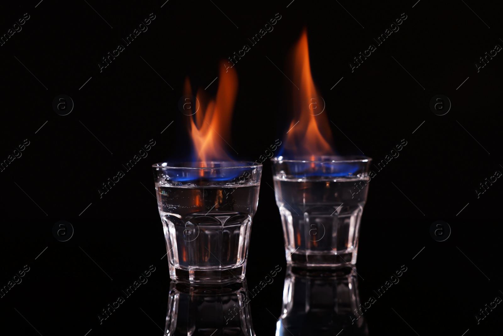 Photo of Flaming vodka in shot glasses on black background