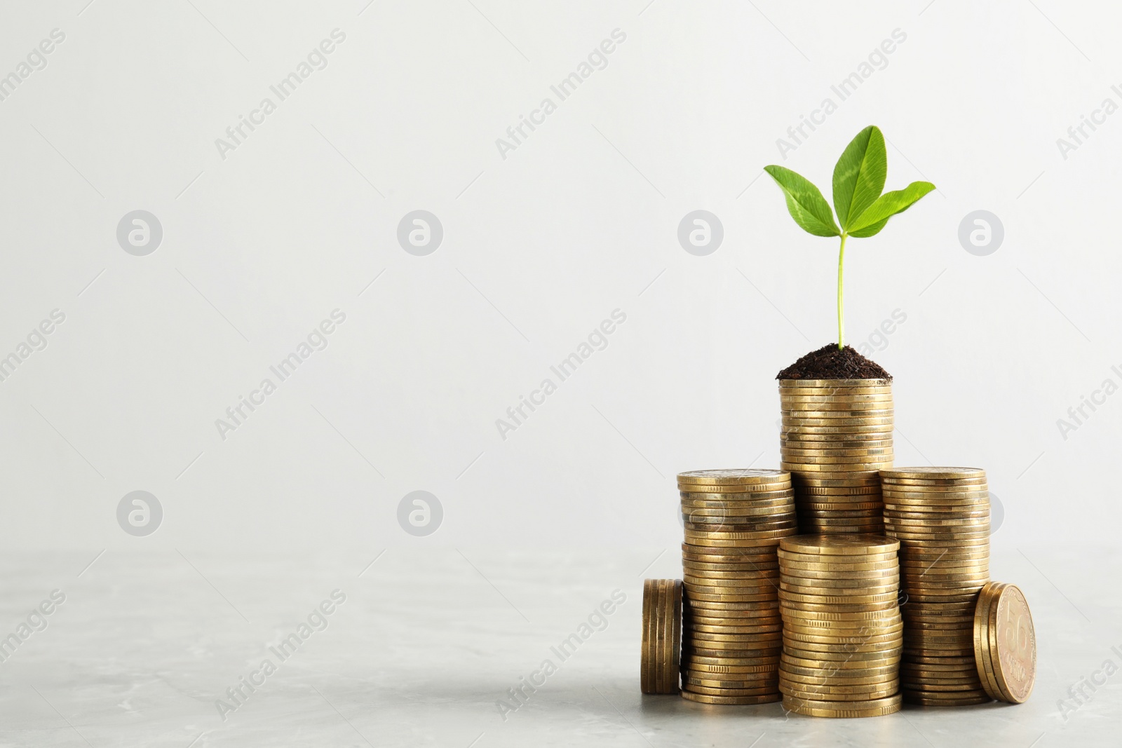 Photo of Stacked coins and green sprout on white marble table, space for text. Investment concept