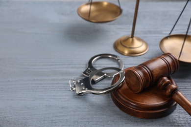 Photo of Gavel, handcuffs and scales of justice on grey wooden table, space for text. Criminal law