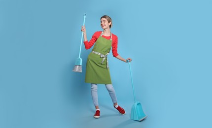 Photo of Young housewife with broom and dustpan on light blue background