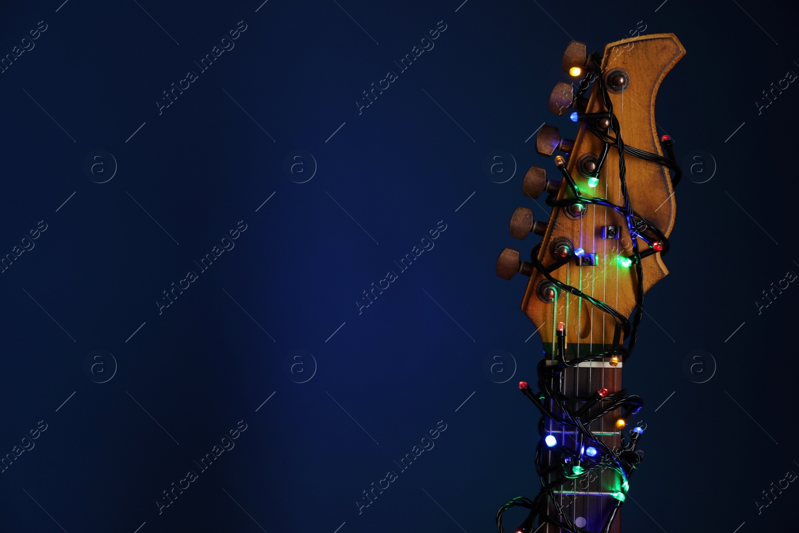 Photo of Guitar with festive lights on blue background, space for text. Christmas music