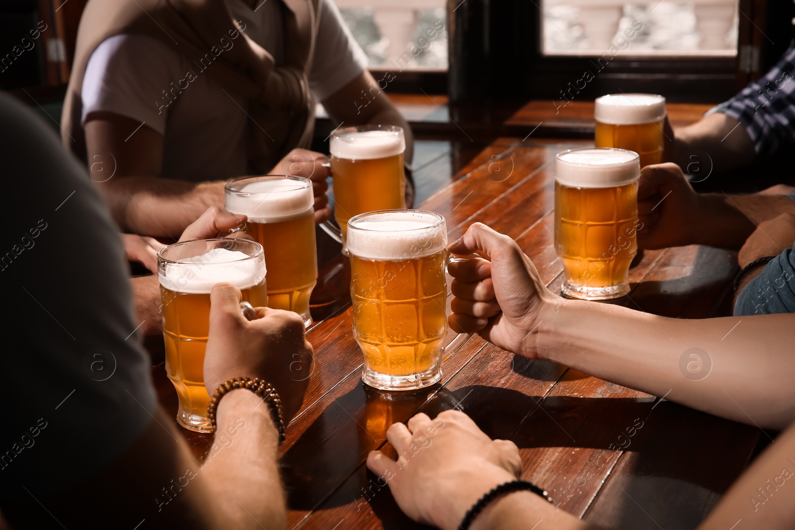 Photo of Friends with tasty beer at wooden table in pub, closeup