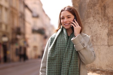 Beautiful woman in warm scarf talking on phone outdoors, space for text