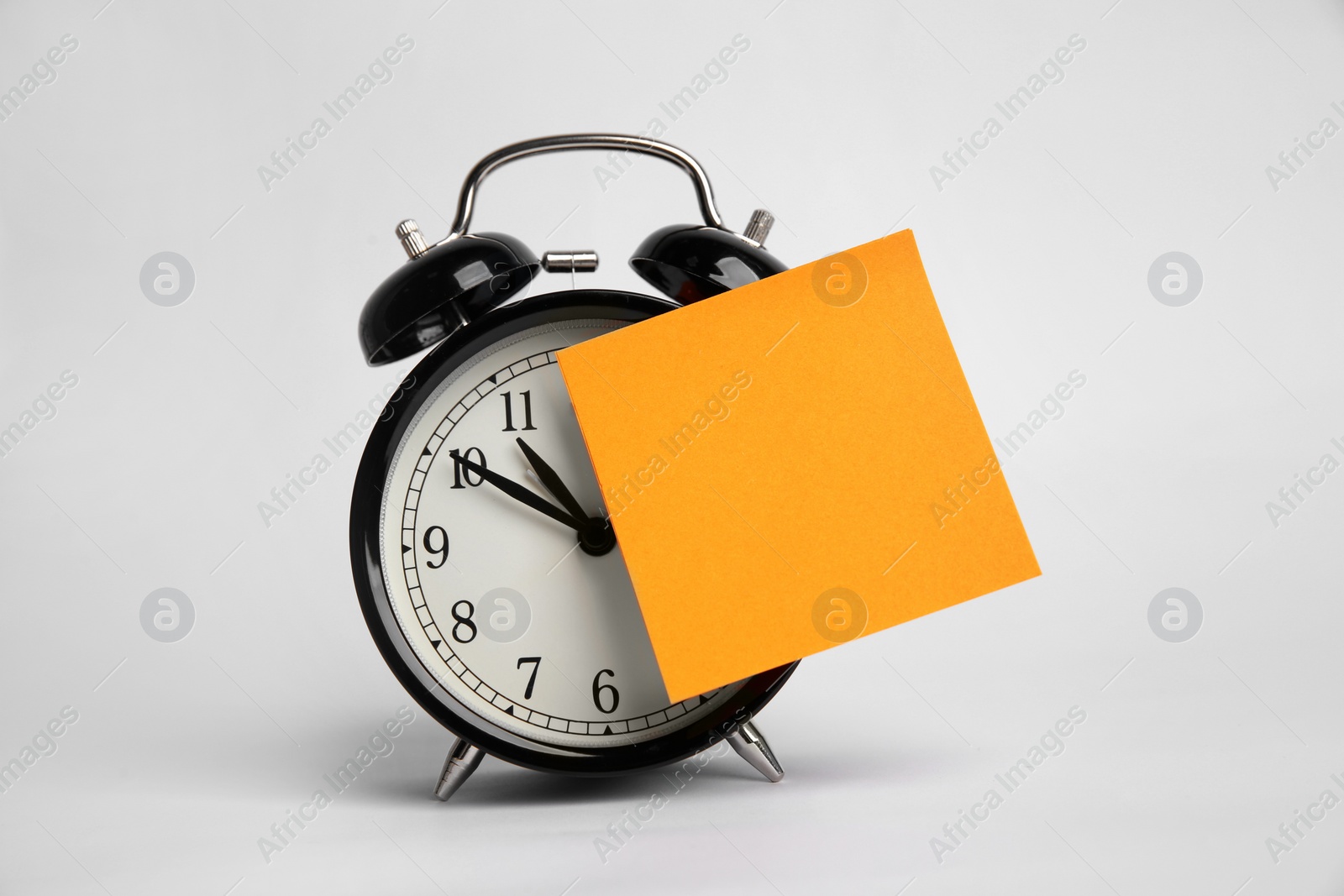 Photo of Alarm clock and blank reminder note on light grey background. Space for text