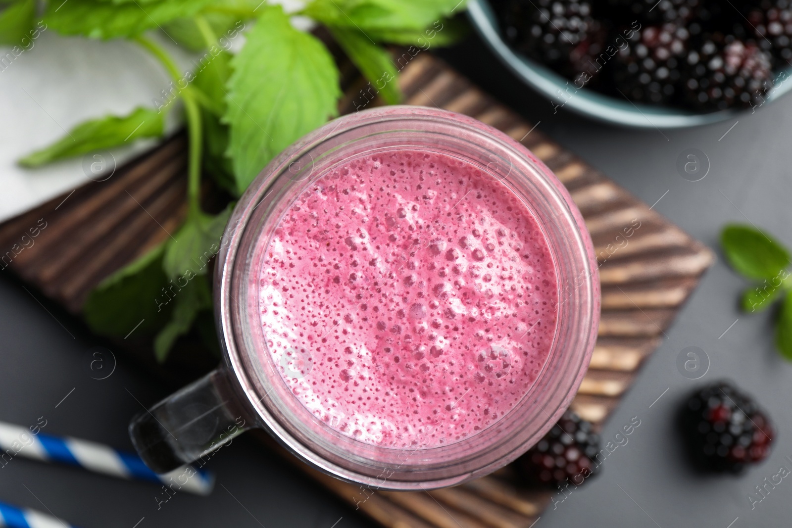 Photo of Mason jar of blackberry smoothie with mint and berries on grey table, flat lay