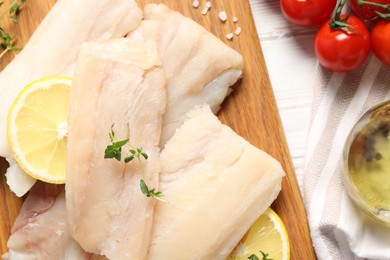 Photo of Pieces of raw cod fish, lemon and tomatoes on white wooden table, top view