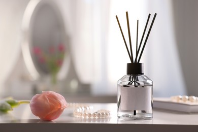 Photo of Reed diffuser, beautiful flower and pearl necklace on white table indoors. Space for text