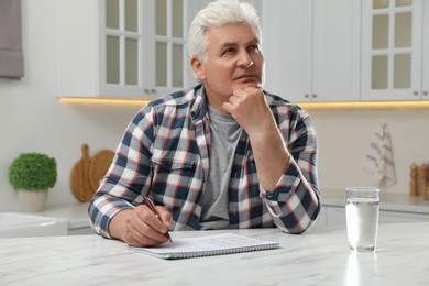 Senior man solving sudoku puzzle at table in kitchen