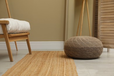Stylish knitted pouf and armchair in room