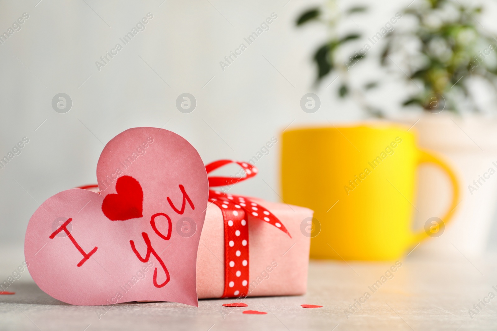 Photo of Heart shaped greeting card with phrase I Love You near gift box on table