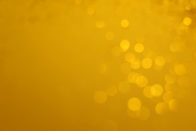 Blurred view of golden lights on yellow background, space for text. Bokeh effect